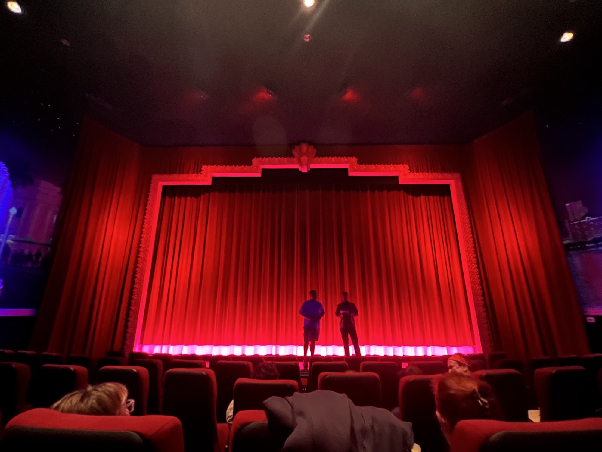 A grand red velvet curtain glowing under footlights across a restored auditorium