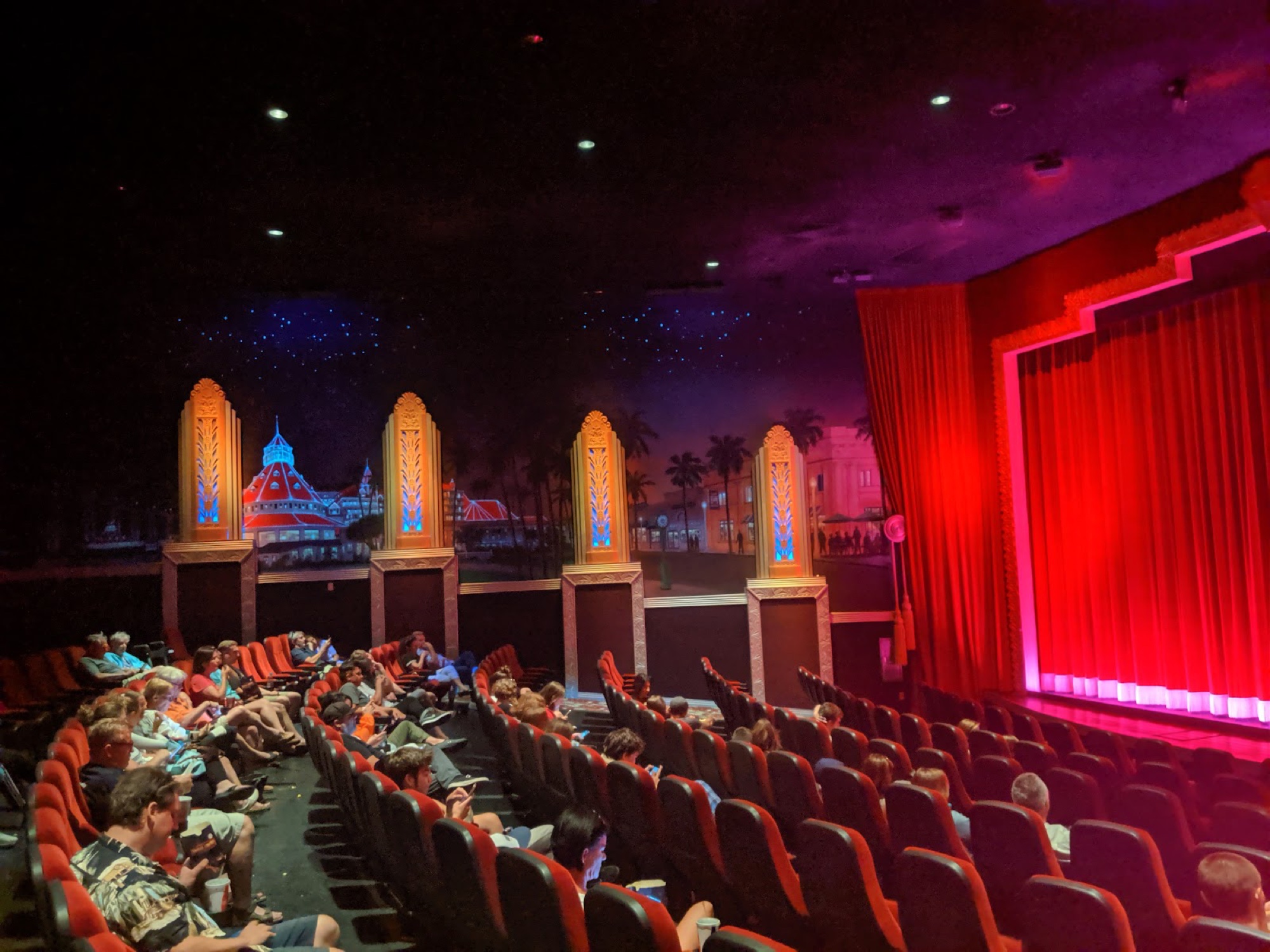 A Village Theatres auditorium lit warm beneath the painted Hotel del mural and illuminated pylons
