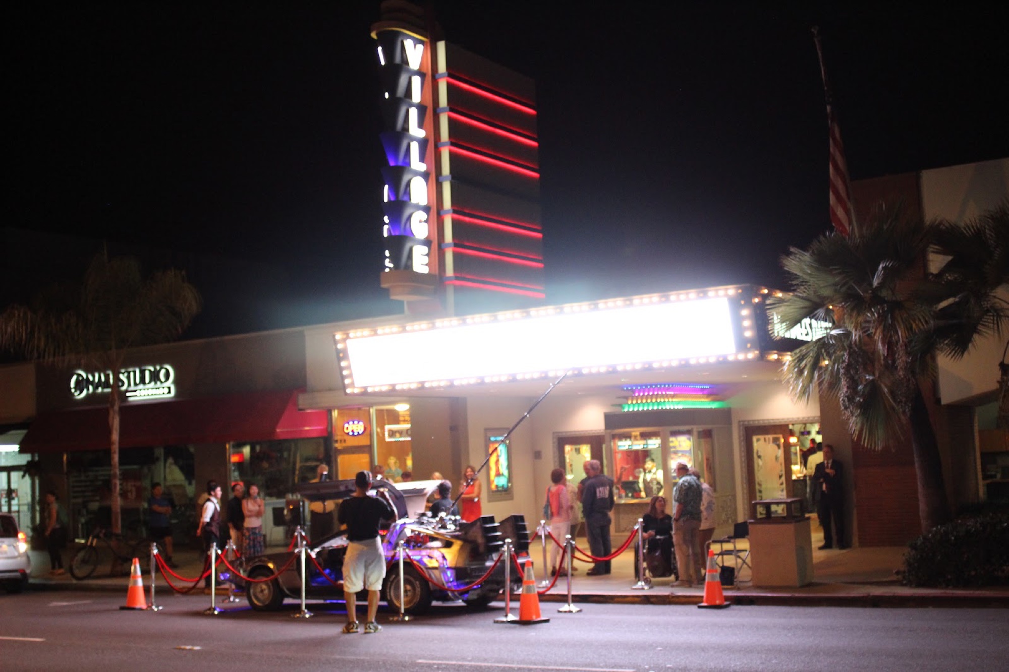 The Village Theatres at night, its tall red-neon VILLAGE tower and lit marquee glowing over the Coronado sidewalk